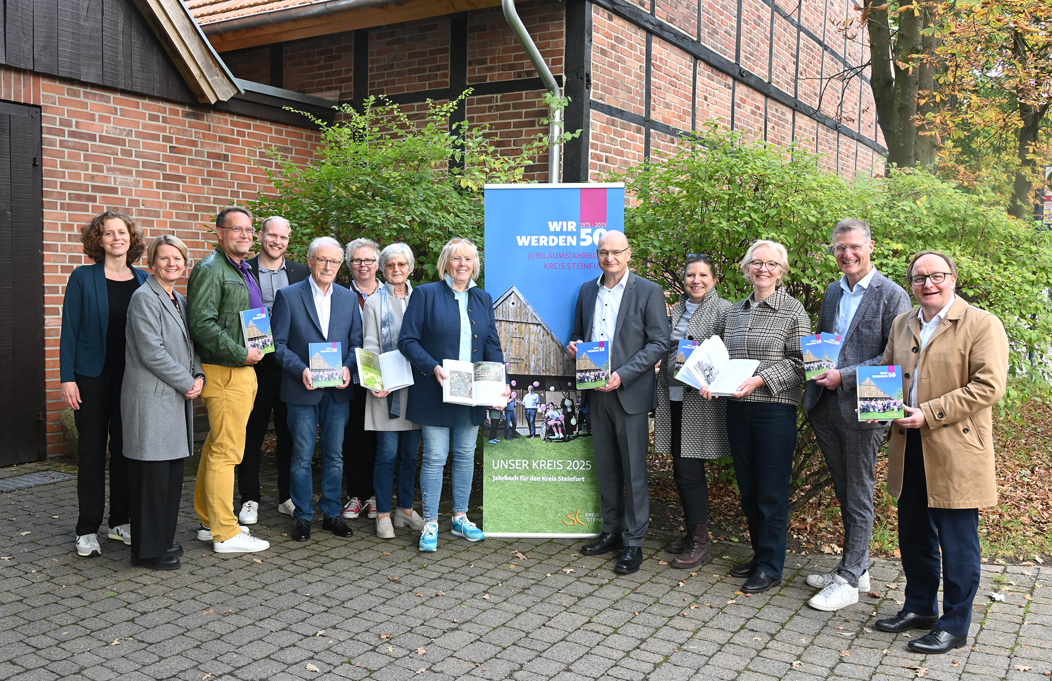 Vertreterinnen und Vertreter der Heimatvereine, Dr. Sommer und Vertreterinnen des Amts für Kultur stehen vor der Bürgerscheune Saerbeck und präsentieren das Jahrbuch 2025.